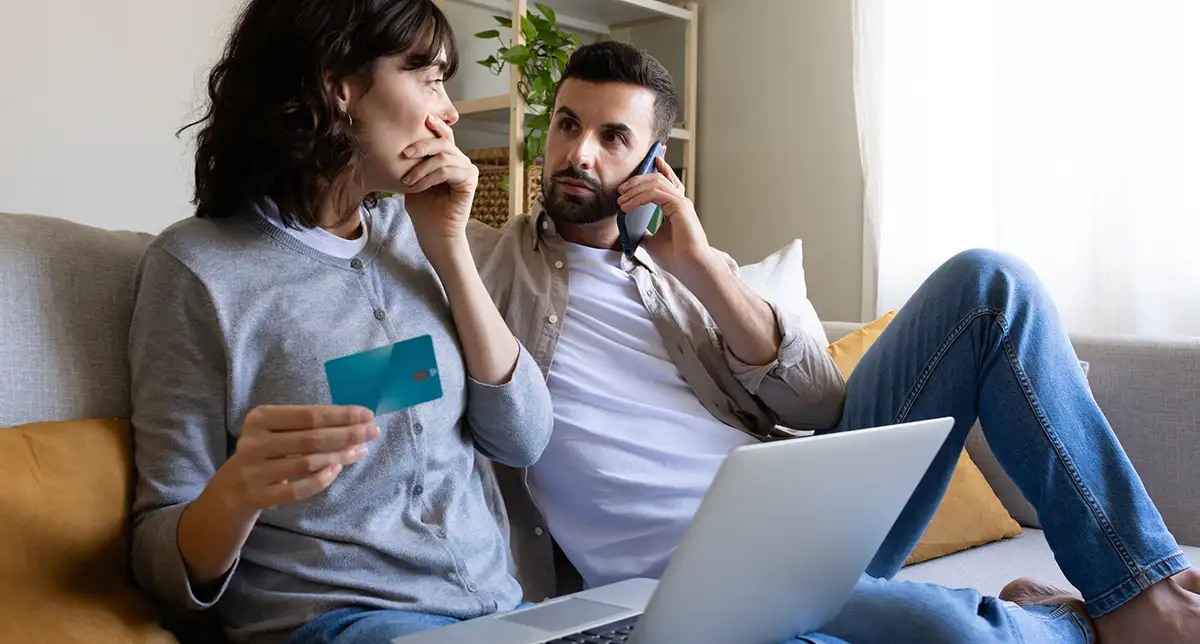 A young couple sitting on the sofa with their laptop worried that they've just fallen victim to fraud